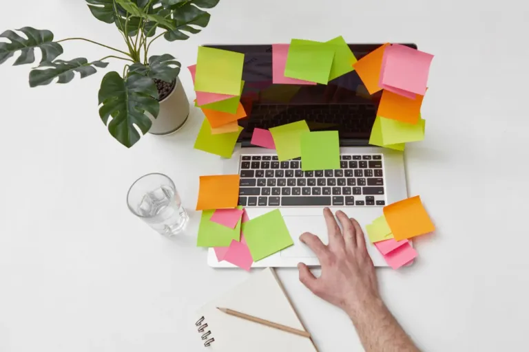 Laptop helemaal beplakt met kleurige memobriefjes op een wit bureau naast een plant
