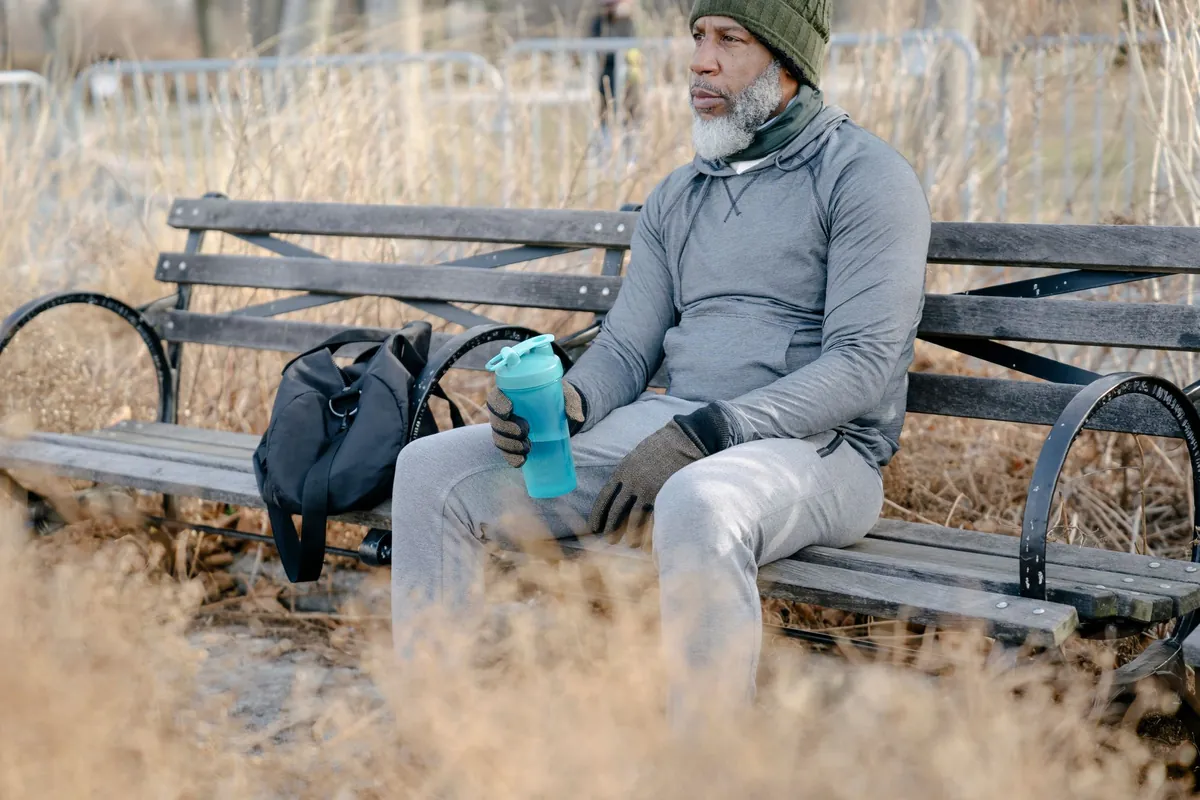 Man zit uit te rusten op een bankje in een veld met een waterfles in zijn hand