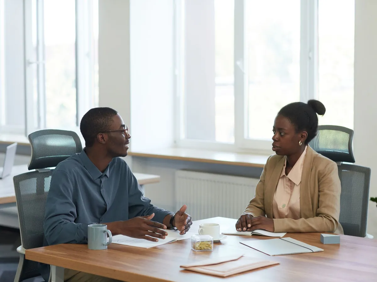 Twee collega's in gesprek aan een tafel in een licht kantoor