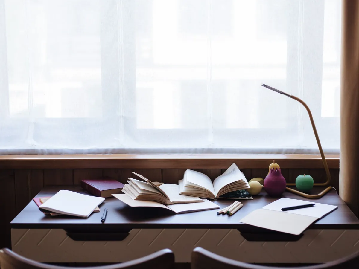 Licht bureau bij het raam met opengeslagen boeken en notitieblokken