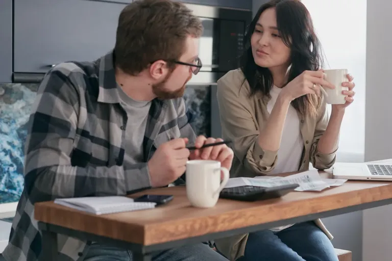 Man en vrouw zitten samen aan de keukentafel en praten rustig met een kop koffie