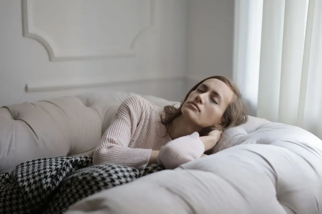 Vrouw ligt met gesloten ogen uit te rusten op een lichte bank onder een deken