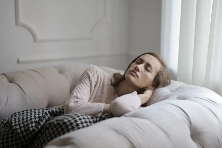 Vrouw ligt met gesloten ogen uit te rusten op een lichte bank onder een deken