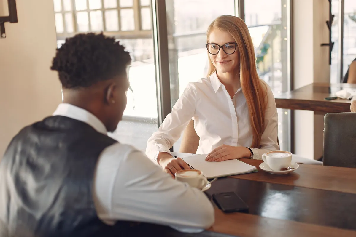 Twee mensen in een rustig gesprek aan tafel met koffie in een licht kantoor